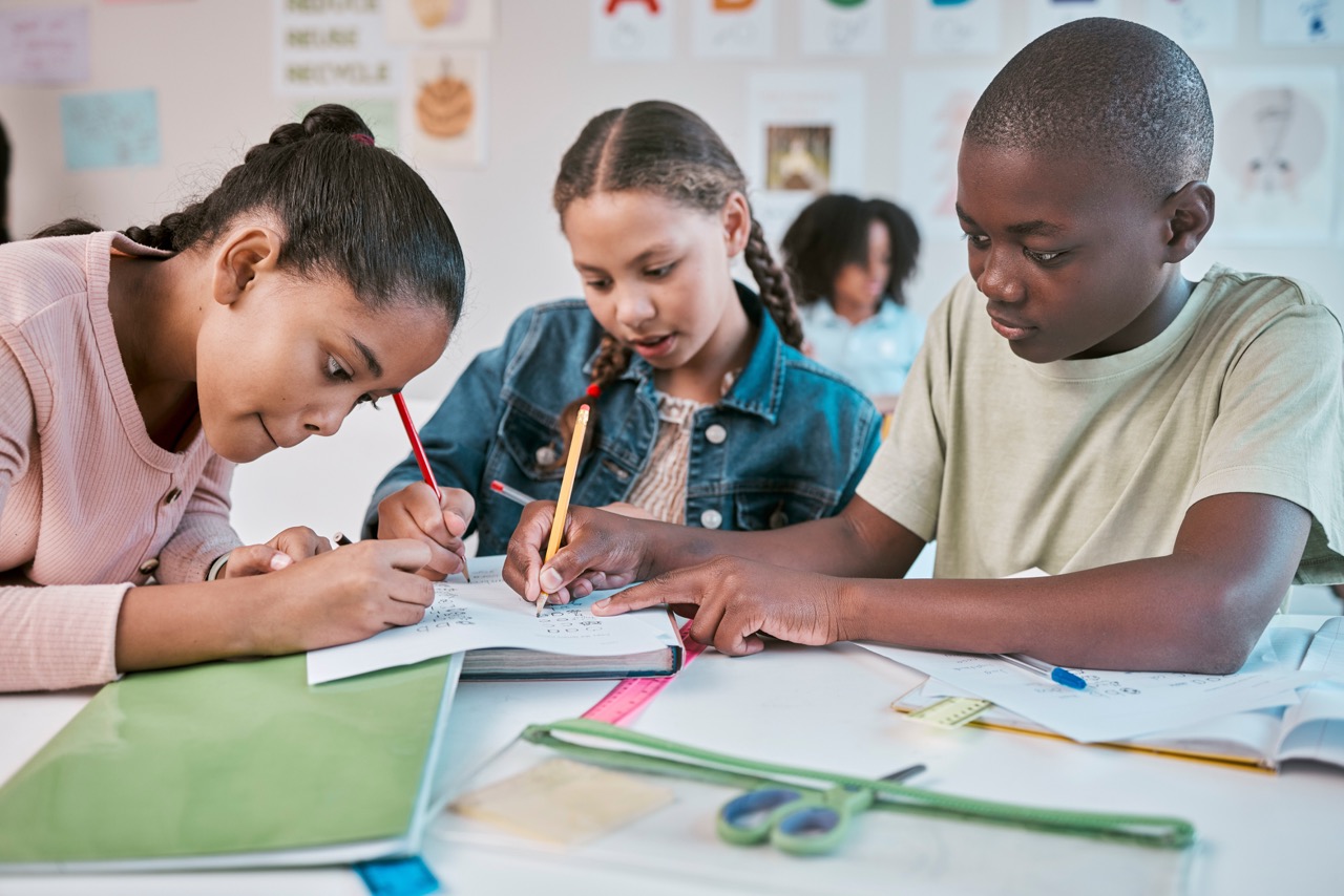 Students working together at a classroom table with notebooks  